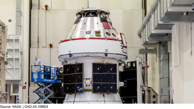 Two workers on a lift next to the Orion Multi-Purpose Crew Vehicle inside a building.
