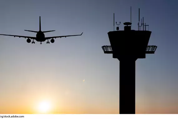 Photo showing a plane flying in the distance and an air traffic control tower in the forground.