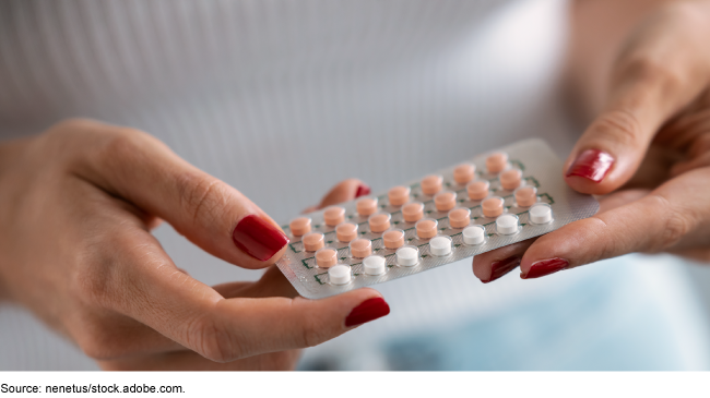 Close up of a person's hands with painted red fingernails holding a pack of oral contraceptives Close up of a person's hands with painted red fingernails holding a pack of oral contraceptives
