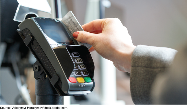 A hand swipes a card through a retailer's payment terminal. 