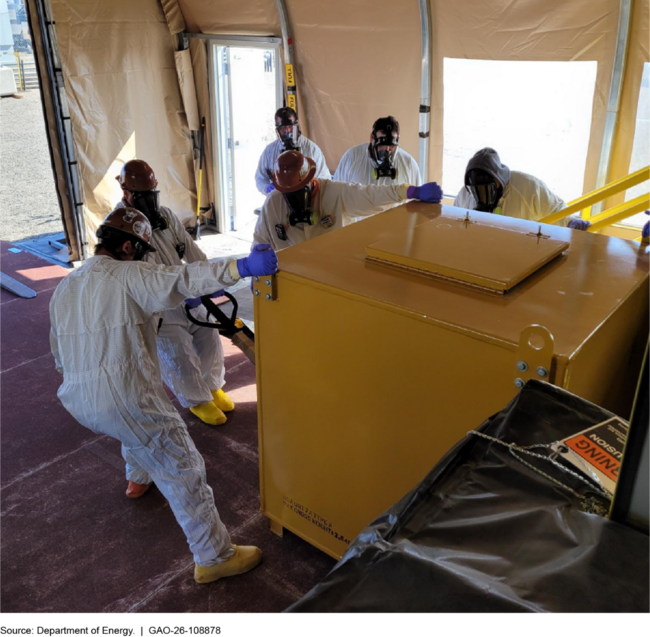Workers in clean-suits and gas masks pull at a large, heavy-looking steel container Workers in clean-suits and gas masks pull at a large, heavy-looking steel container