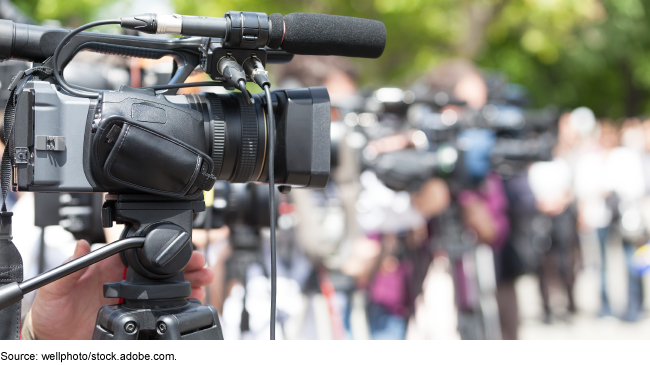 A video camera in focus with other cameras and people blurred in the background.