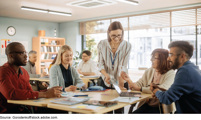 A group of people in a classroom talking while sitting in groups.