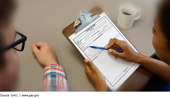 This is a photo of a woman and man seated at a table looking at a counseling form attached to a clipboard.