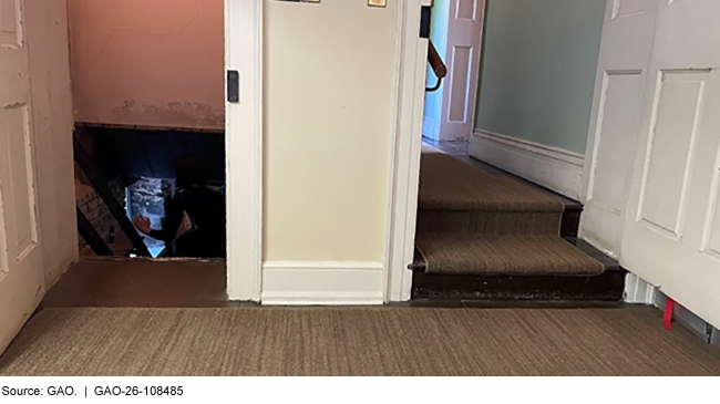 A photograph taken inside a museum in a historic house, showing a doorway leading to a hallway 2 steps up and another doorway to a basement. 