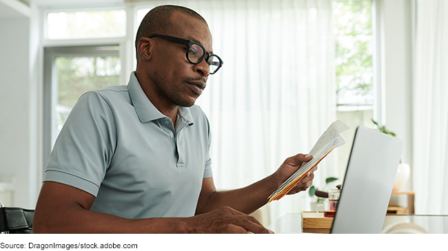 A man holding papers while looking at a laptop.