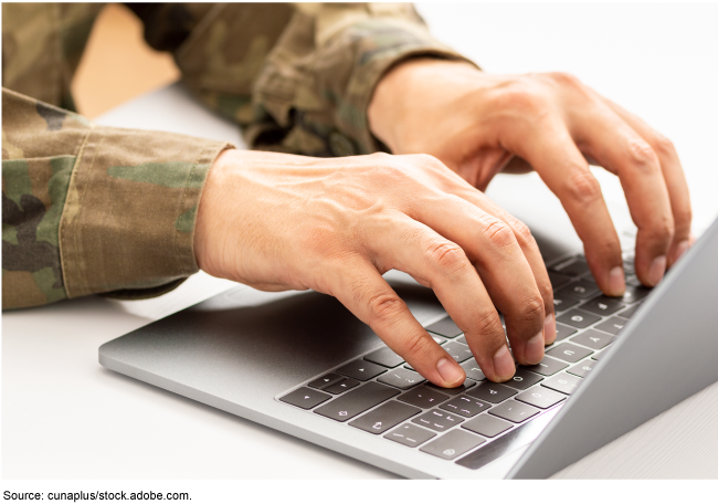 A person in military fatigues typing on a computer.