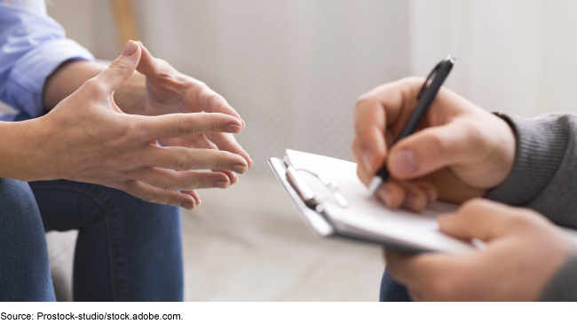 Hands of two people sitting across from one another; one is taking notes.