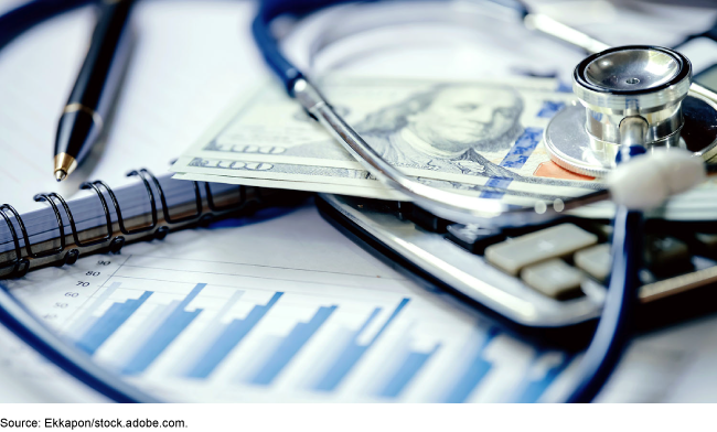 An image of a stethoscope, a hundred-dollar bill and other office items on a desk. 