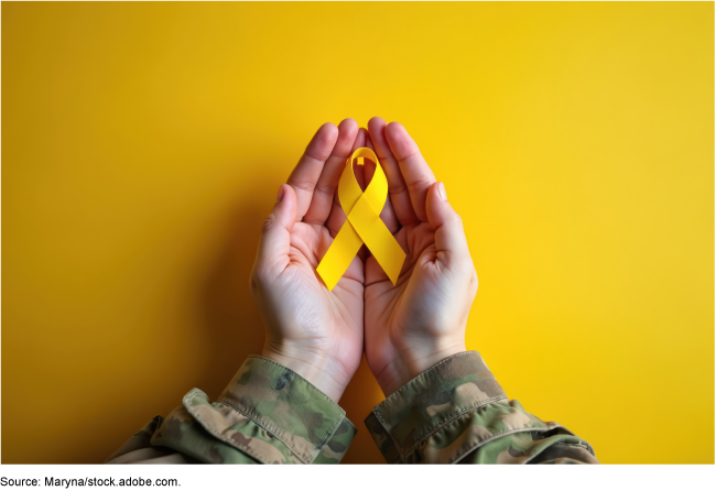 Hands from a person wearing a military uniform hold a yellow ribbon, symbolizing hope and military support.  