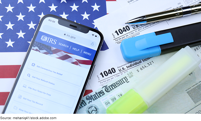 Tax documents, pens, and an iPhone on the official IRS website on a background of the U.S. flag.