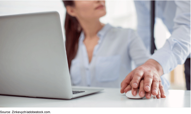 A woman sitting in front of a laptop holding a computer mouse with another person's hand laying on top of hers.