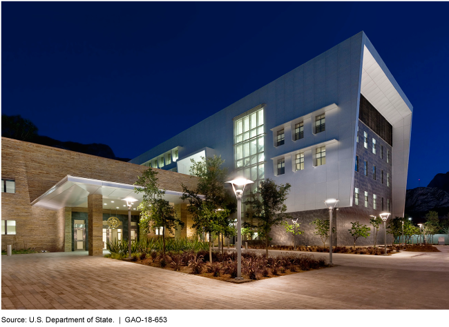 Picture of a modern building with a brick entryway at night with lights and plantings.