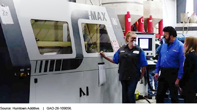 Three people standing beside a large 3D printer in a warehouse