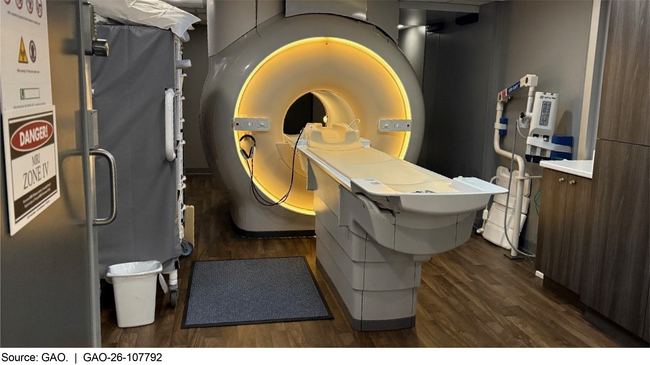 An MRI machine, which looks like a medical exam table positioned at the opening of a large plastic cylinder with a hole large enough for the exam table to enter.