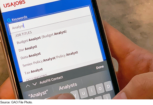 Someone holding a cellphone with the keywords search on the USAJobs website displayed on the phone's screen.