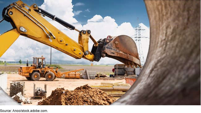 Earthmoving equipment at a construction site viewed through a section of pipe.