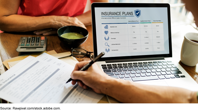 A person sitting across from someone taking notes and looking at a laptop displaying insurance plans.