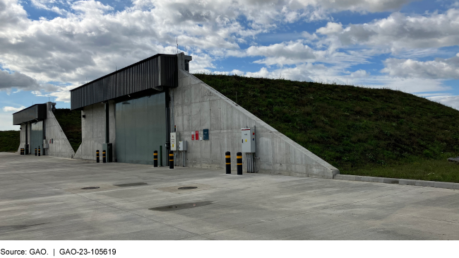 Photo showing two munitions storage bunkers. They have concrete fronts with large metal doors and are covered with grass on top.