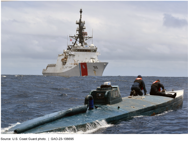 Two Coast Guard personnel on top of a vessel in open water with a large Coast Guard ship in the background.