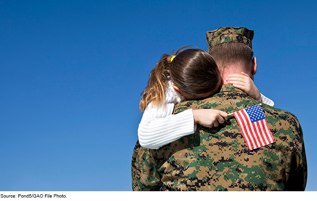 A servicemember in fatigues holding a child with a small American flag in her hand.