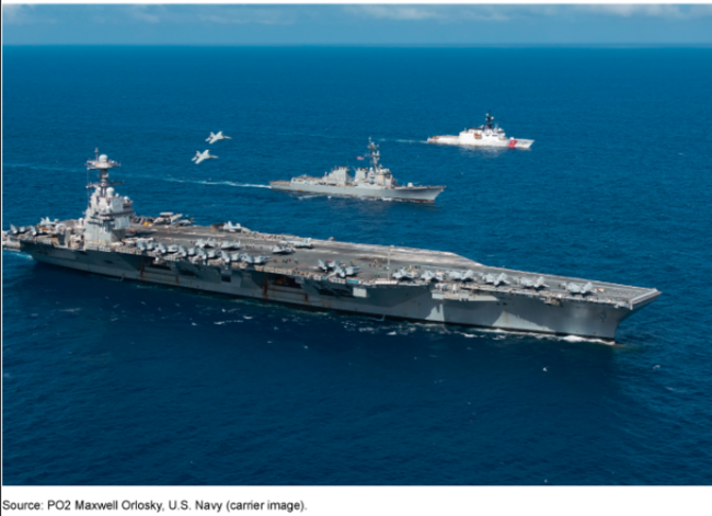 An aircraft carrier in the ocean with jets overhead and other ships nearby