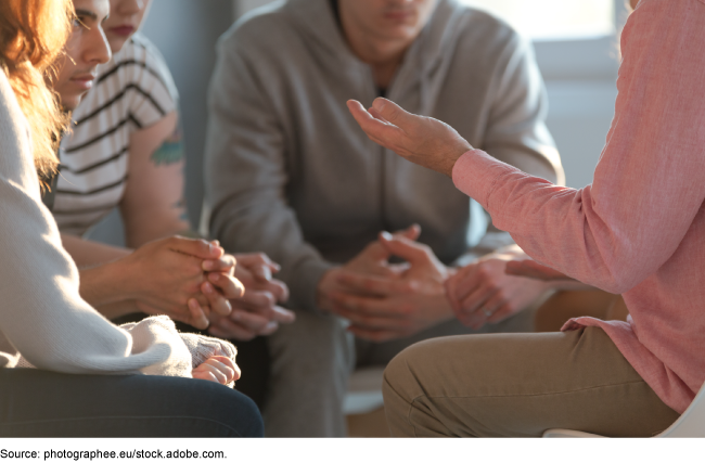 A diverse group of young adults sitting next to each other in a tight circle talking
