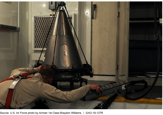 Photo of a technician examining cone-shaped piece of missile on a table. 