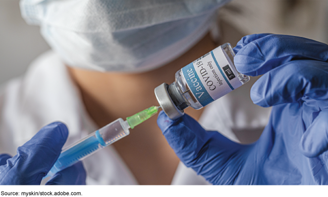 Medical professional using a syringe to withdraw the COVID-19 vaccine from a vial.