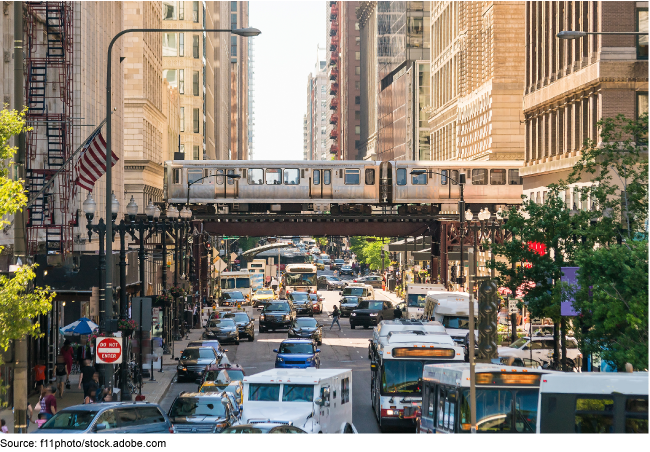 A downtown cityscape with tall buildings, rail transit, cars, and people.