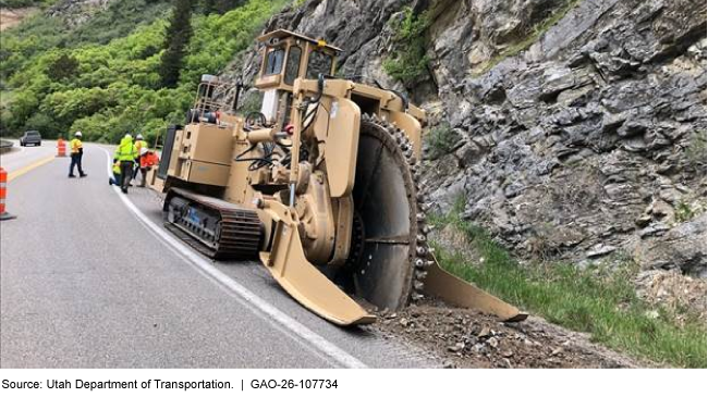 Several construction workers operate a larger trencher to excavate along the shoulder of a highway through a canyon.