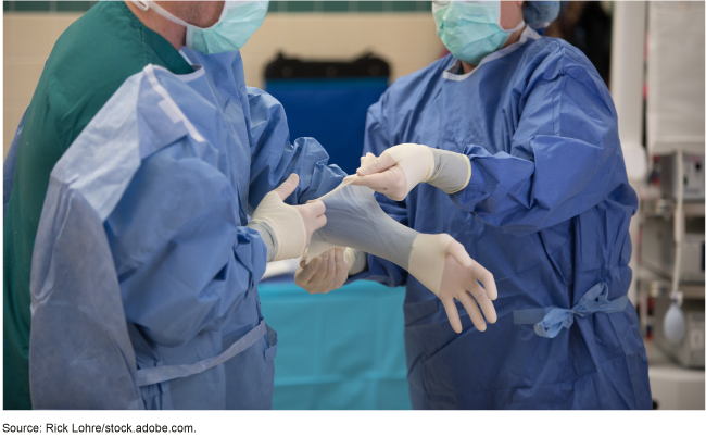 A person wearing scrubs assists another person place their rubber gloves over the sleeve of their scrubs.