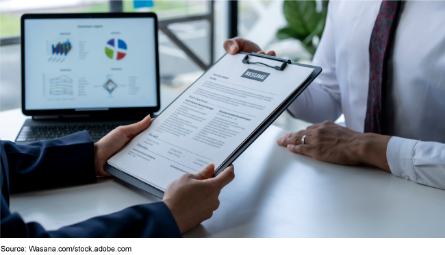 A person holding a resume in front of a computer. 
