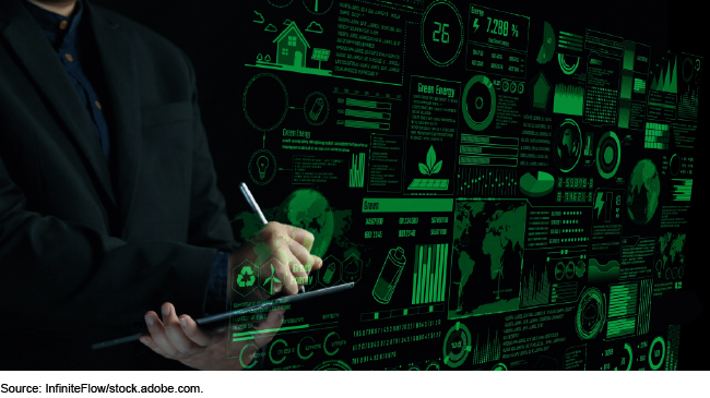 A person writing on a tablet in the background with a digital dashboard projection from the laptop of schematics, data, and numbers related to finances and renewable energy