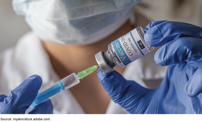 Healthcare worker uses a syringe to extract COVID-19 vaccine from a vial.