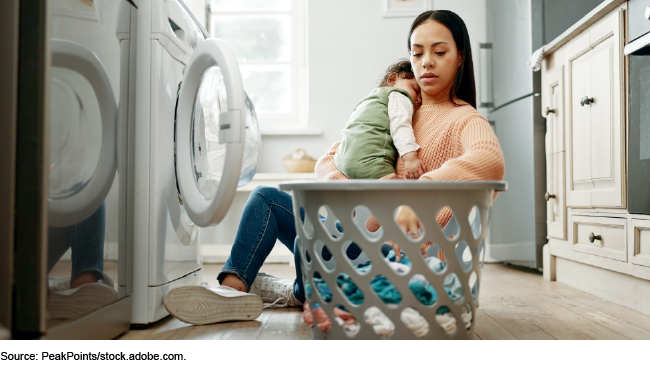 A woman holding a baby sitting on the floor doing laundry A woman holding a baby sitting on the floor doing laundry