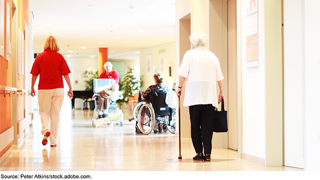 An image of a nursing home lobby, showing residents and workers in a hallway near elevators. 