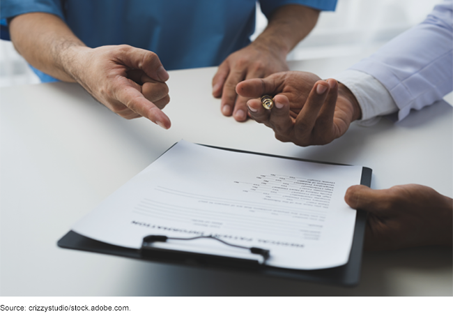 Two people at a table. One is holding a clipboard with a form on it and the other is pointing at the form.