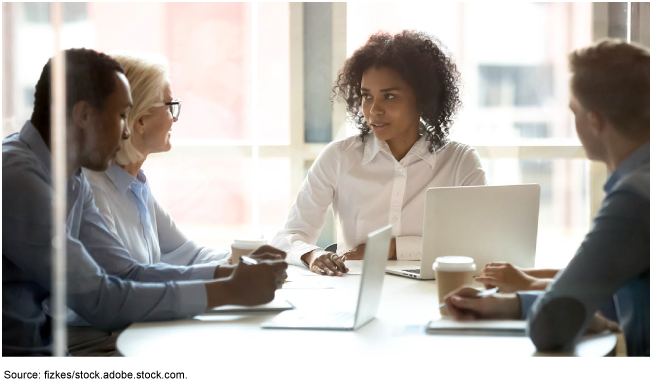 Four diverse individuals meeting around a table with windows in the background.