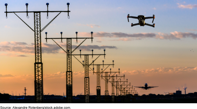 Runway lights at an airport with an airplane in the background and an airborne drone in the foreground.