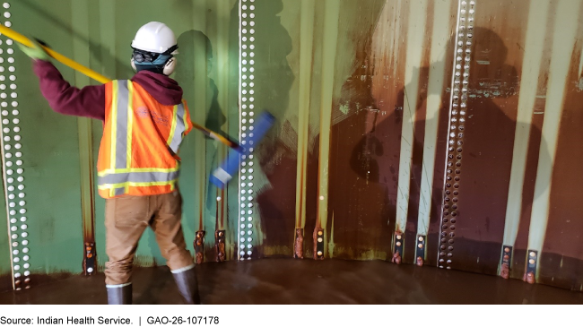A person inside of a large water storage tank using a broom to clean the walls. 