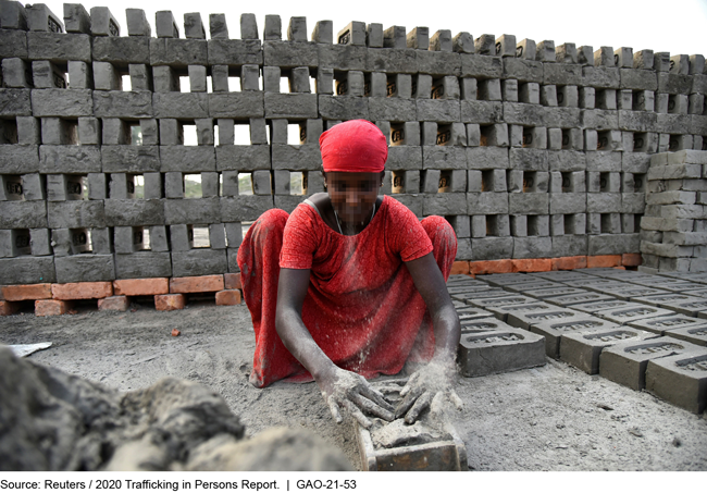 Woman in a red dress making bricks inside of an outdoor brick structure.