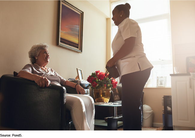 A home care worker greeting an older, seated woman 