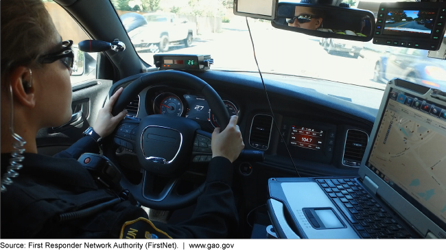 A police officer driving a cruiser with a laptop displaying a map 