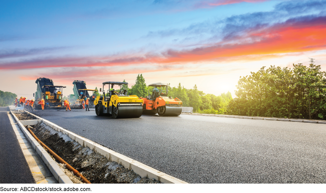 Construction workers and equipment for laying and smoothing out asphalt for a road.