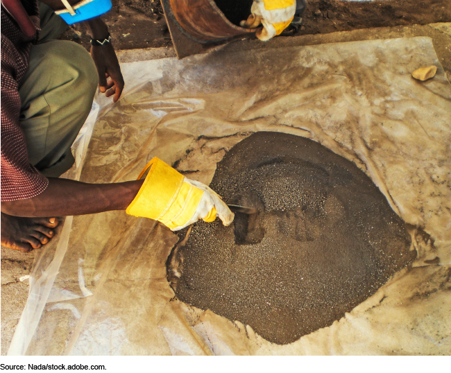 A person wearing gloves and a mask and mining coltan ore