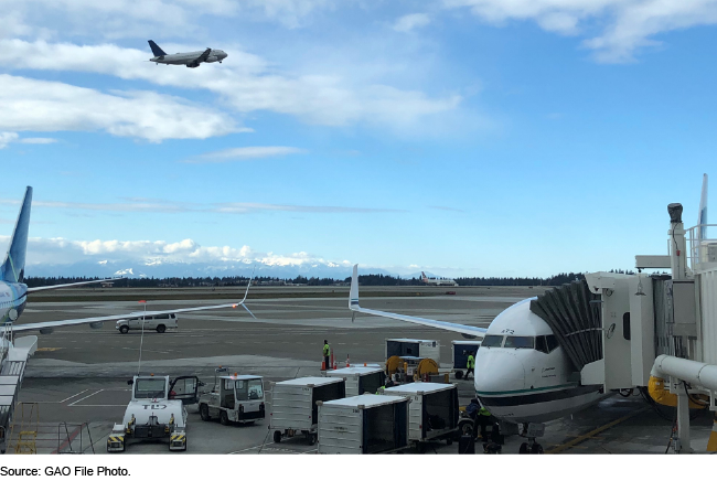 Two passenger airplanes parked at a terminal with an airplane overhead in the sky.