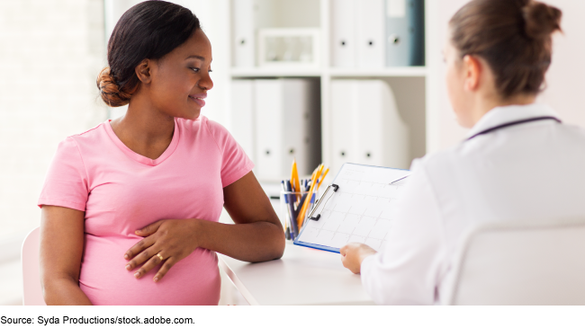 A pregnant person sitting in front of a person wearing a white medical coat and holding a clipboard. A pregnant person sitting in front of a person wearing a white medical coat and holding a clipboard.