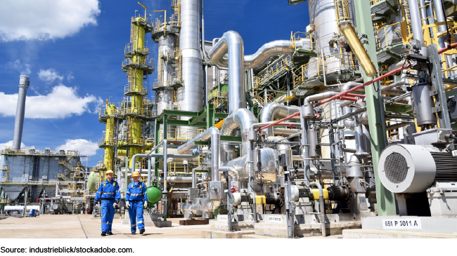 Chemical facility with pipes and two workers in blue jumpsuits and yellow hard hats. Chemical facility with pipes and two workers in blue jumpsuits and yellow hard hats.