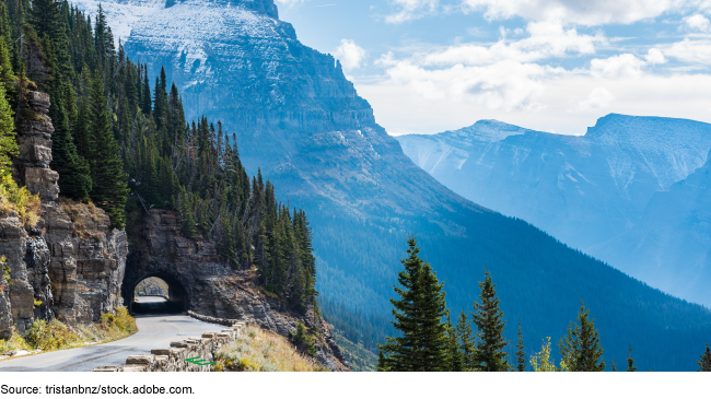 Natural underpass on the side of a mountain with vast mountains in the background.